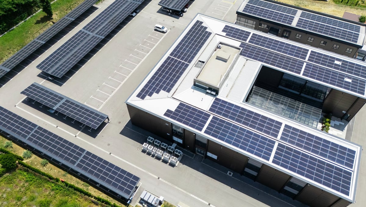 Aerial view of building with solar panels on a roof and parking space with solar canopies. Business office building.