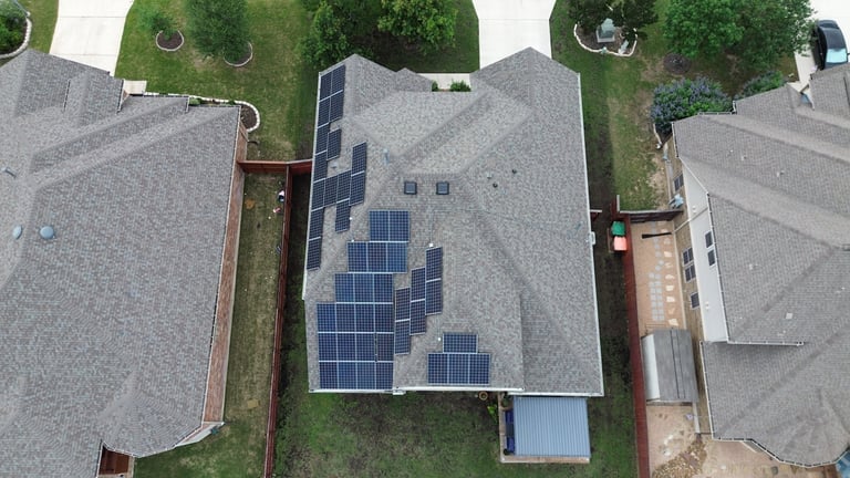 Aerial view of residential house with solar panels installed on roof, surrounded by green lawn and neighboring homes