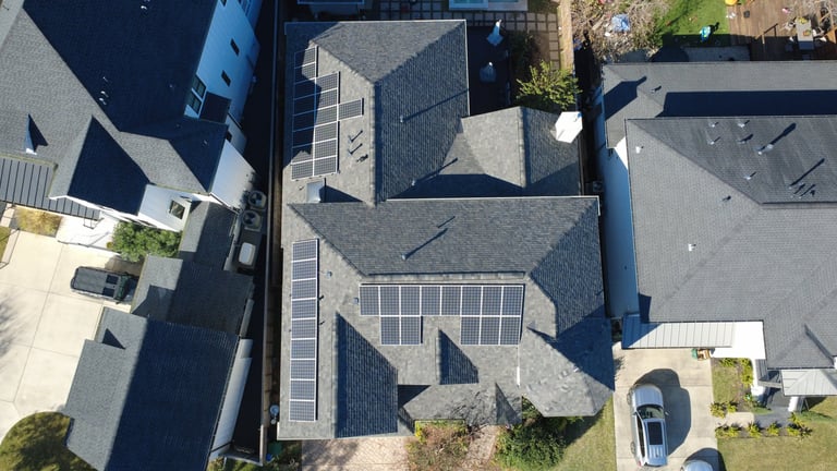 Aerial view of residential home with gray tile roof, solar panels, and driveway with parked car