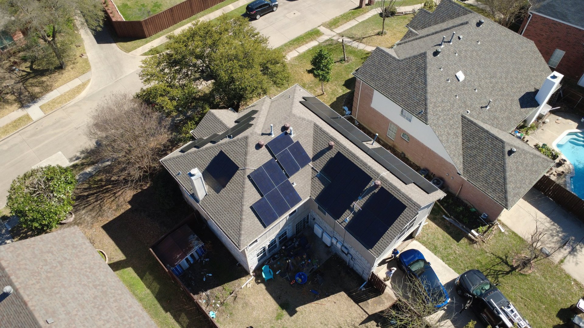Aerial view of a residential home with solar panels on the roof and a two-car garage in a suburban neighborhood.