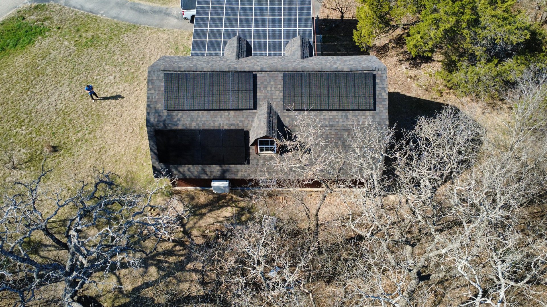 Aerial view of a modern house with solar panels on the roof, surrounded by arid landscape and sparse vegetation