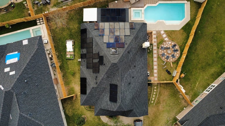 Aerial view of a residential home with dark shingle roof, surrounded by manicured lawn, two pools, and yellow property lines