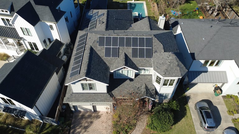 Aerial view of residential home with solar panels on roof and driveway with parked car