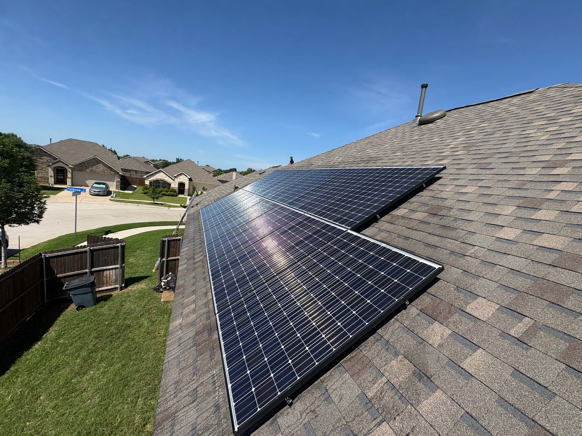 Solar panels installed on a residential roof with houses and green lawn visible in a suburban neighborhood