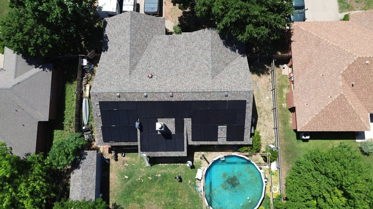 Aerial view of a modern house with a dark roof and circular blue swimming pool, surrounded by trees and neighboring homes