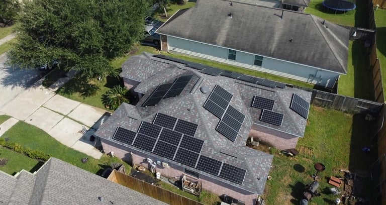 Aerial view of residential house with solar panels installed on roof, surrounded by green lawn and trees
