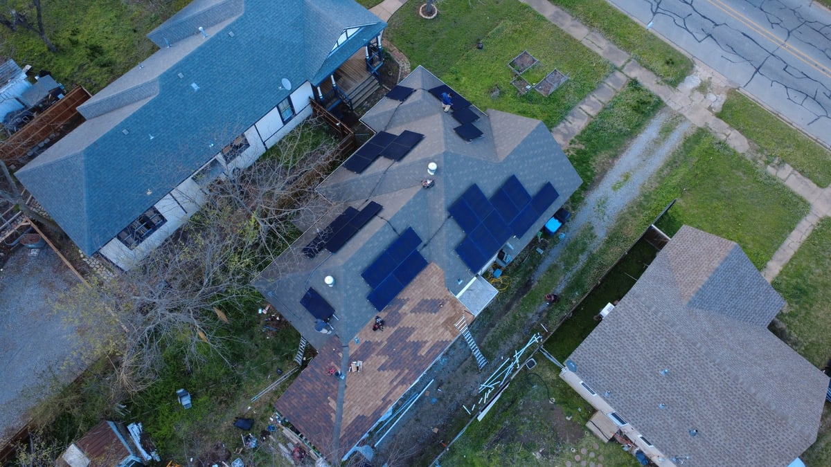 Aerial view of residential property with blue-roofed building, solar panels, and surrounding green spaces