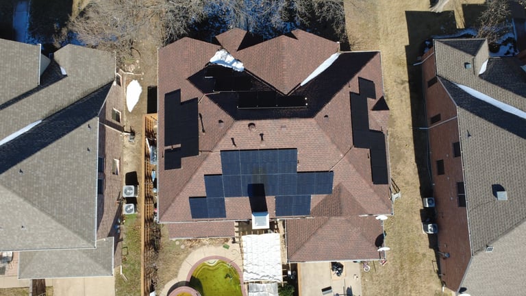 Aerial view of a house with solar panels installed on the brown roof and driveway below