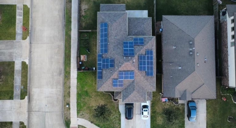 Aerial view of residential rooftop with blue solar panels installed on the house, showing driveway and adjacent properties