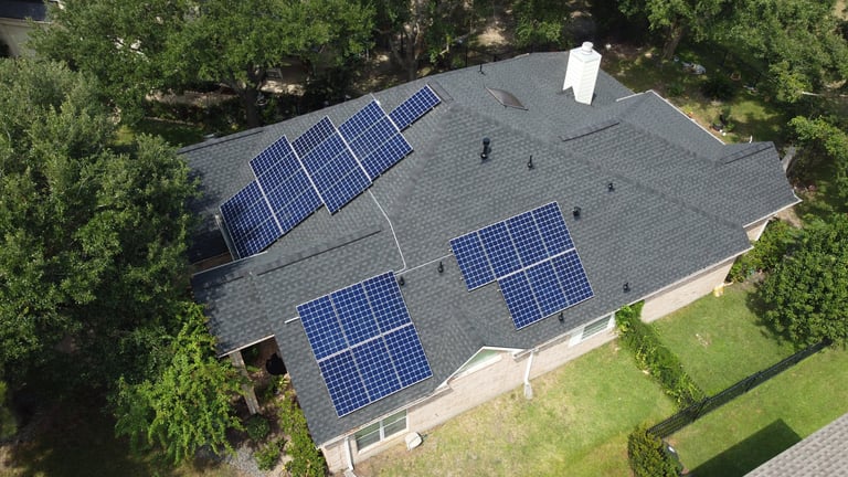 Aerial view of a residential house with solar panels installed on the roof, surrounded by green trees and lawn