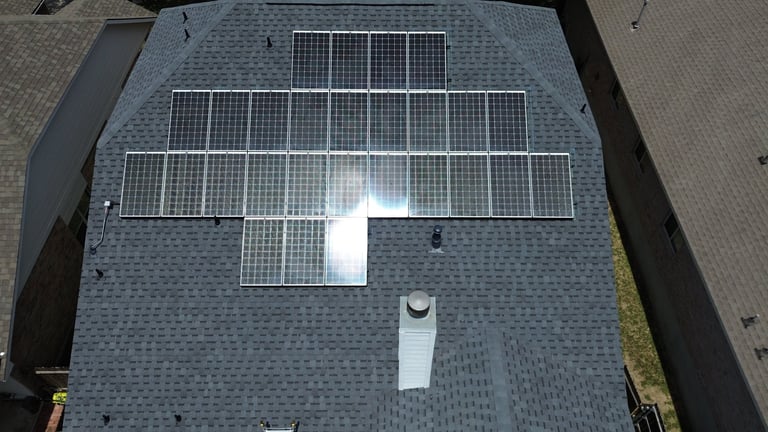 Aerial view of a residential roof with multiple solar panels installed on a gray asphalt shingle surface
