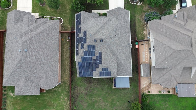Aerial view of three residential houses with roofs, including one with solar panels installed