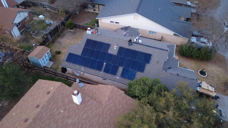 Aerial view of residential property with solar panels installed on roof, surrounded by trees and driveway