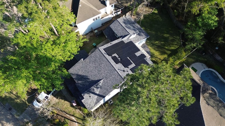 Aerial view of a residential home with dark roof surrounded by lush green trees