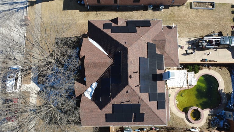 Aerial view of a house with brown and black roof tiles, bare tree, and yard with equipment