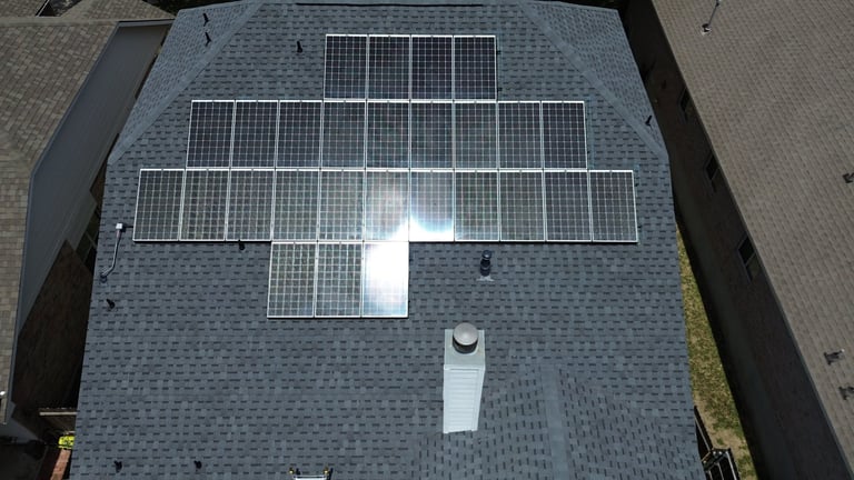 Aerial view of a residential roof with multiple solar panels arranged in rows and a white ventilation unit